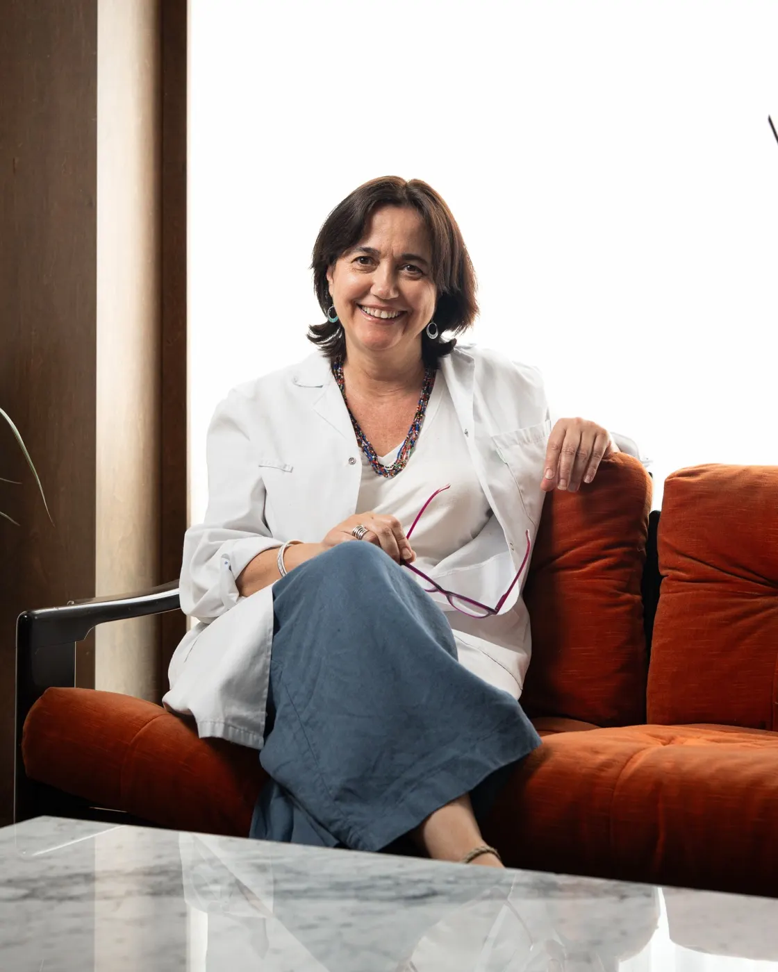 La Dra. Victòria Andreu, amb bata blanca, asseguda als sofàs de la consulta